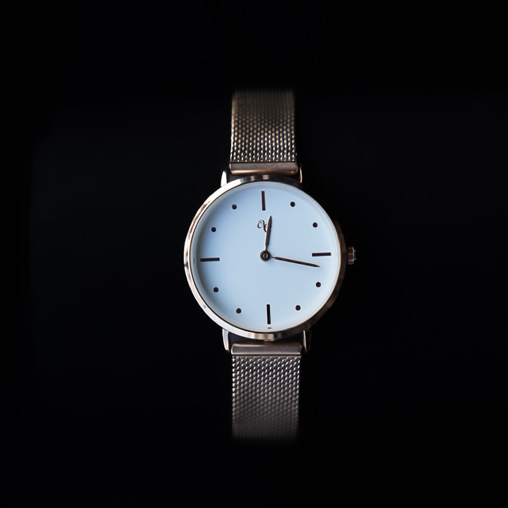 Wristwatch with a white face and rose gold mesh band on a black background